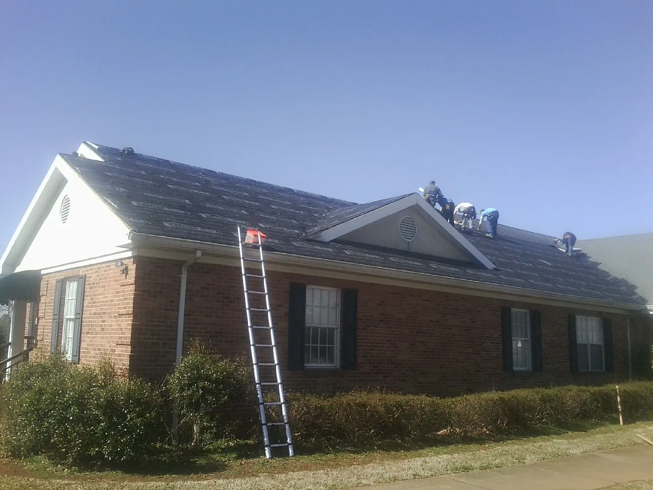 Crew tearing shingles off a brick ranch roof with a ladder set — Emergency Roof Repair work by our crew in Smiths Grove
