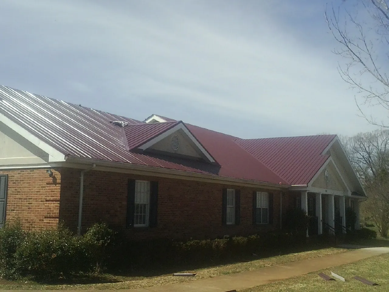 Red metal roof with gabled entries on a long brick building, from a Hail Damage Roof Repair job in Smiths Grove