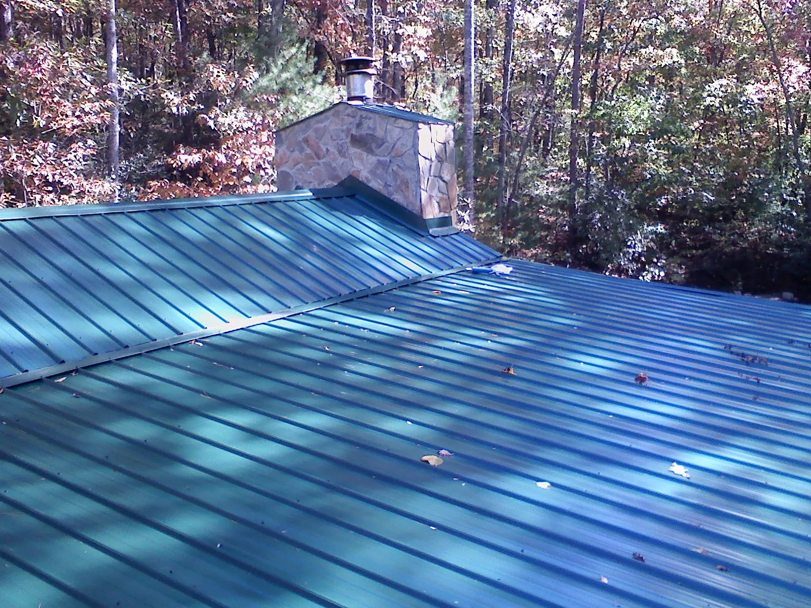 New green metal roof and stone chimney surrounded by autumn woods in Smiths Grove