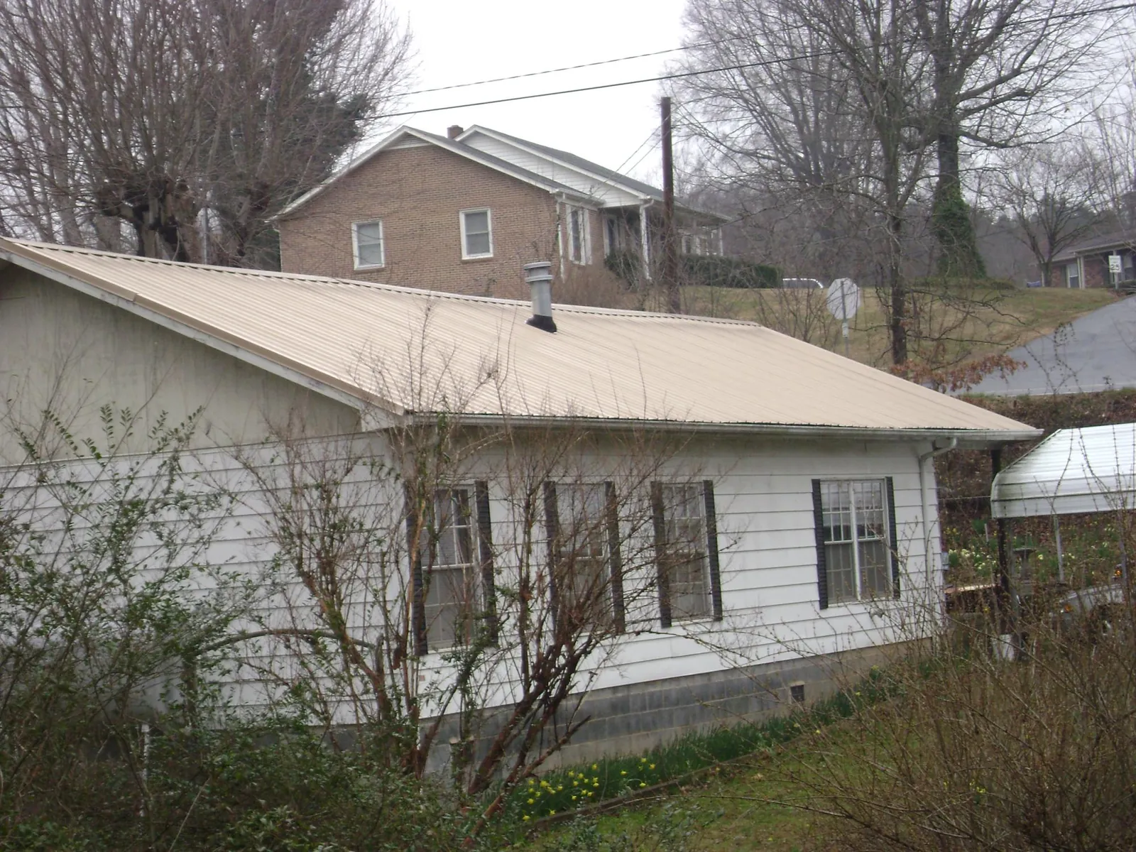 Tan metal roof on a white sided house set into a hillside — Commercial Roofing by Roofing Brothers in Smiths Grove