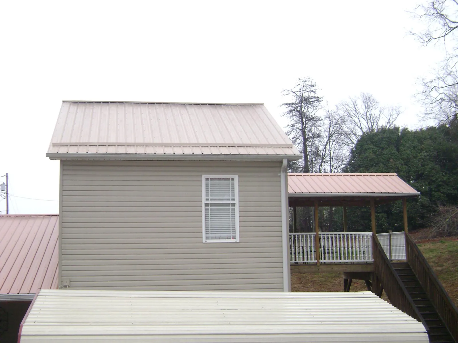 Tan metal roofs on a two story addition and attached porch, from a Roof Replacement job in Smiths Grove